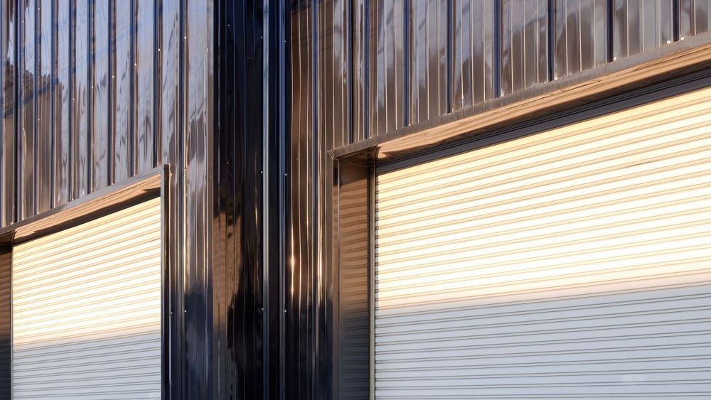 Two brown arched garage doors set into a gray stucco wall, in a driveway.