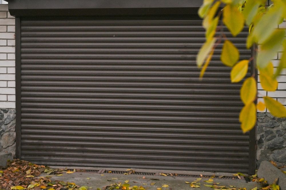 White roll-up garage door in a gray concrete alcove, below gray siding.