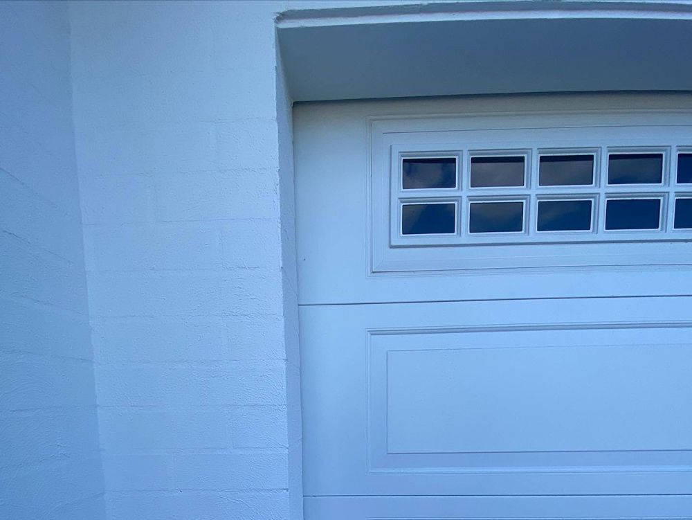 White garage door with window panes. Adjacent white brick wall.