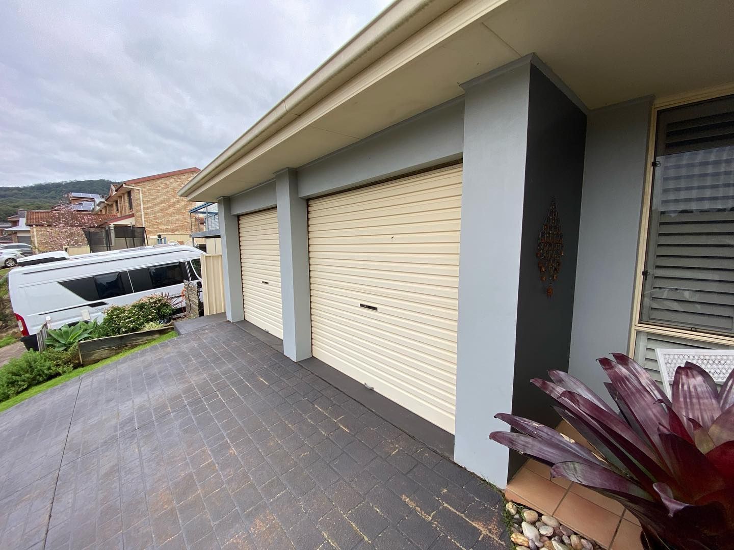 Brick house with cream-colored rolling shutters, green trim, and a blue sky.