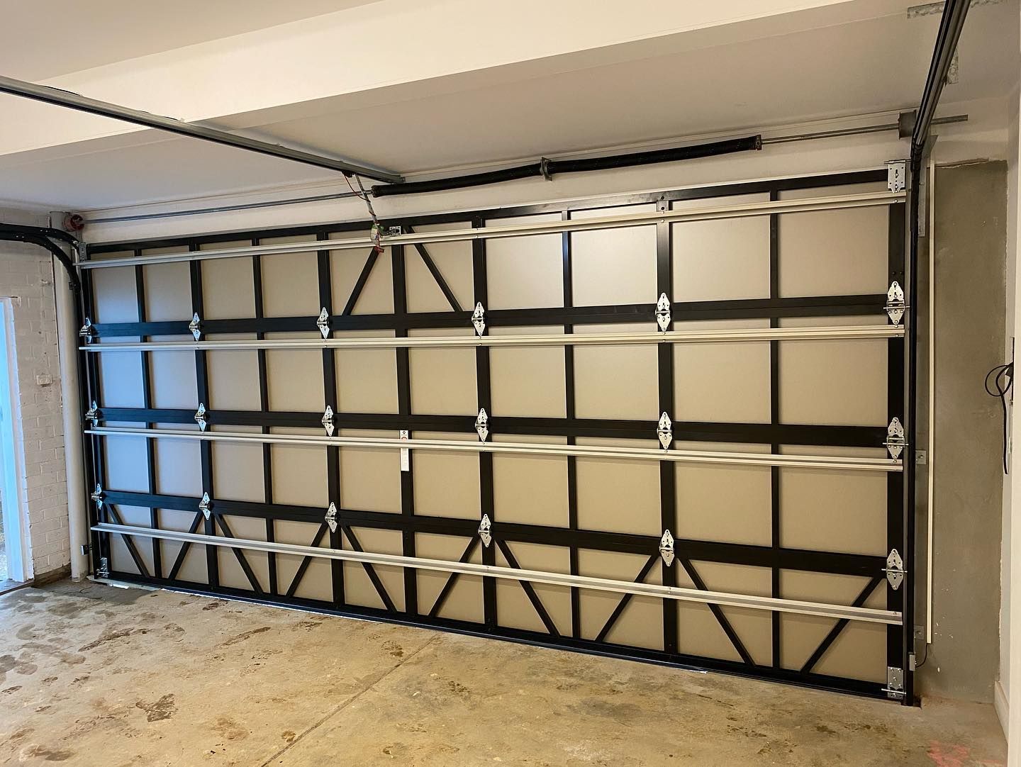 Garage door with black and silver framing and white panels, indoors.