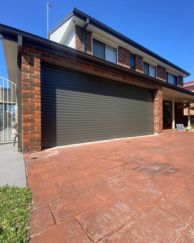 Two-story brick house with a dark brown roll-up garage door and red brick driveway.