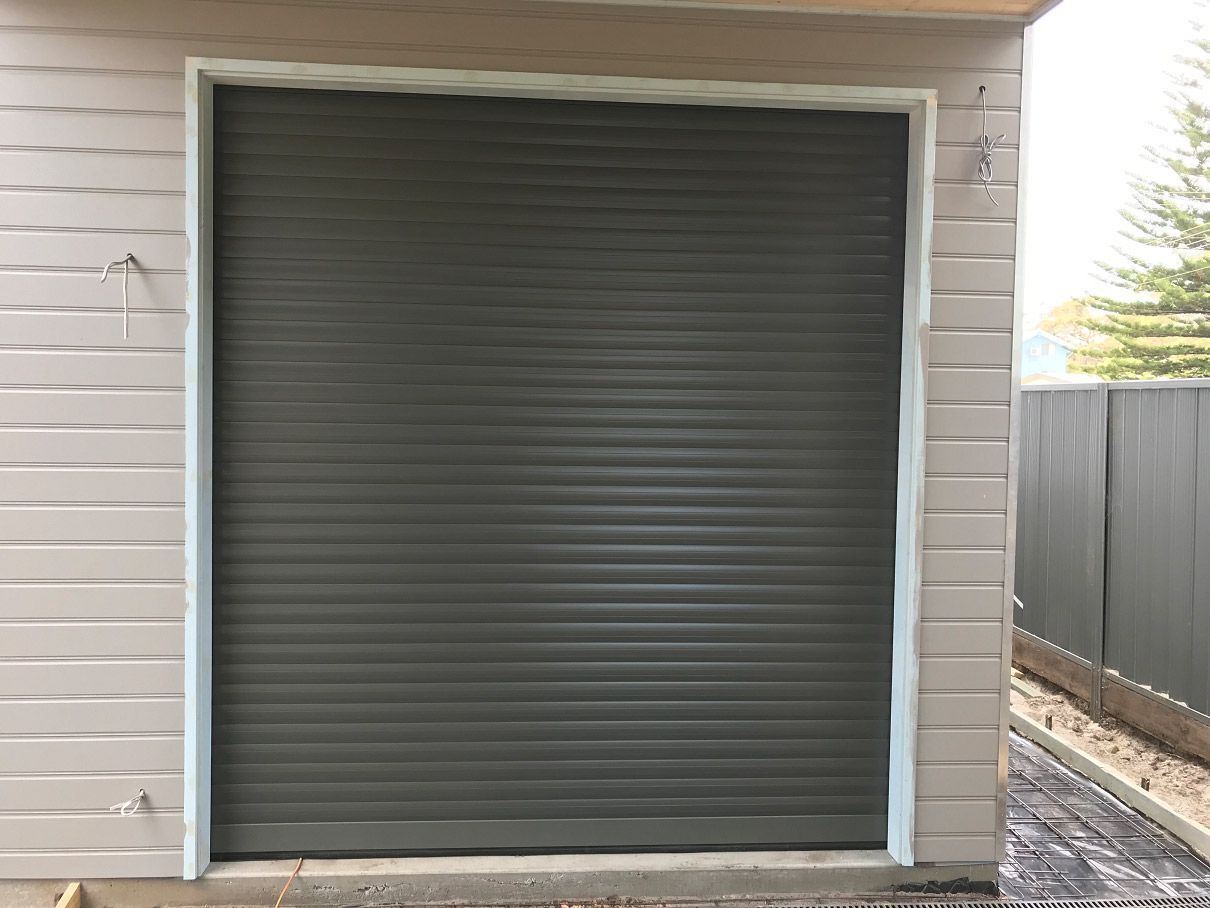 Dark gray rolling shutter door, closed, in a white-walled room.