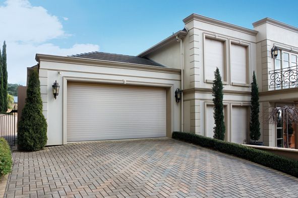 Brick house with brown awnings and roll-down shutters. Green lawn and a blue sky.