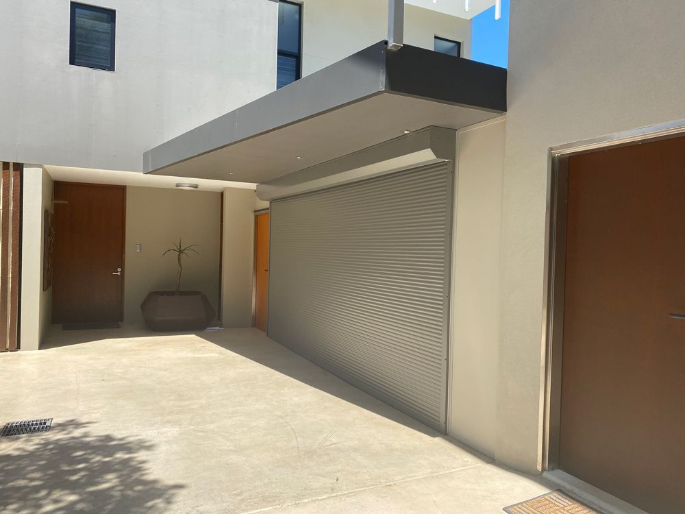 A modern building entrance with a gray awning, roller door, and brown doors on a concrete surface.