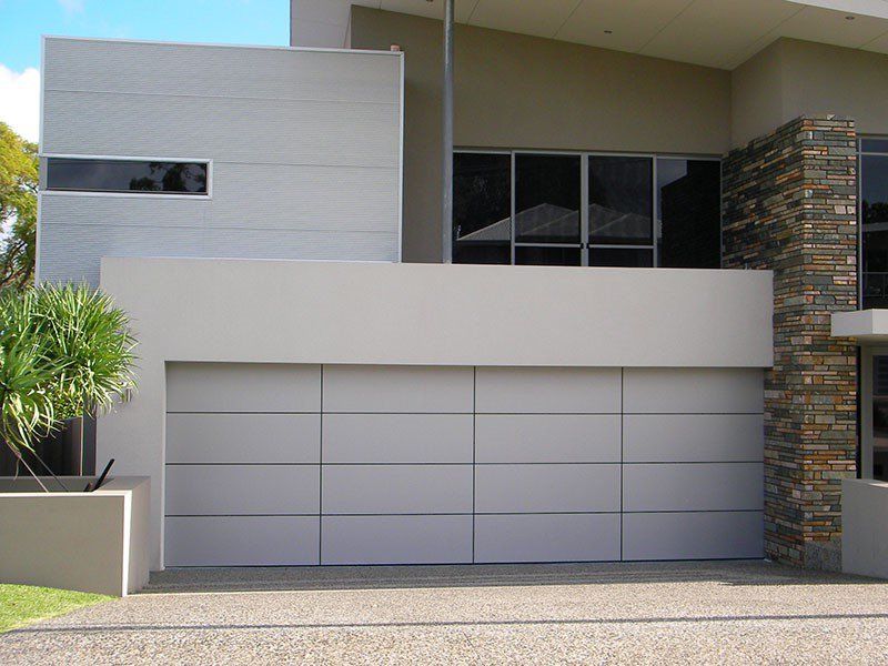 Modern house exterior with glass balcony, brick accents, and metallic garage door.