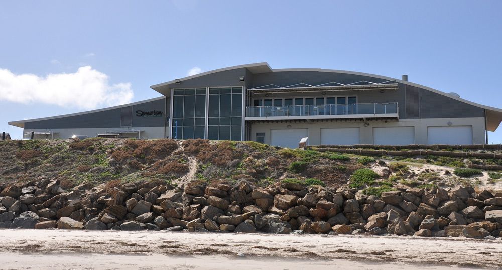 Boat on a trailer inside a garage with a partially open door. White building, boats, bright colors.