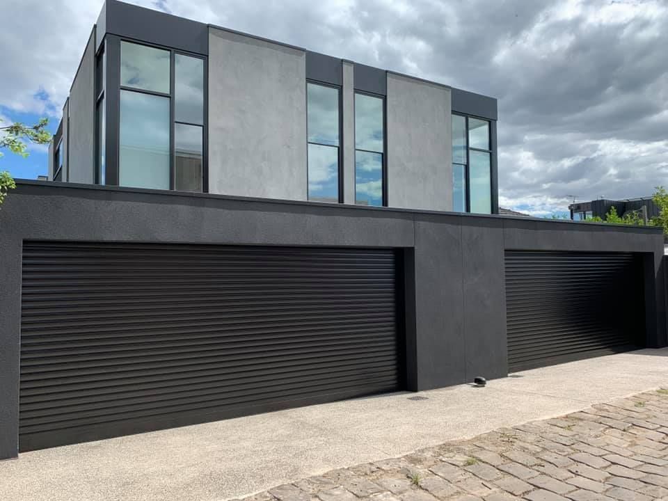 Building with closed, light-colored roll-up door under a silver roof overhang, parked car visible.