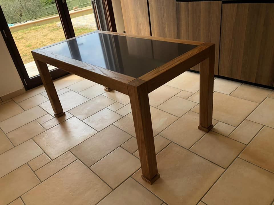 Un tavolo di legno con un piano di vetro nero è appoggiato su un pavimento piastrellato.