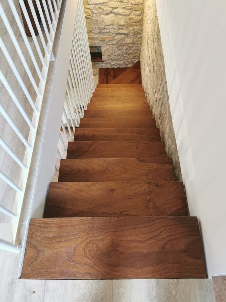 Una scala di legno con ringhiera bianca e muro di pietra.