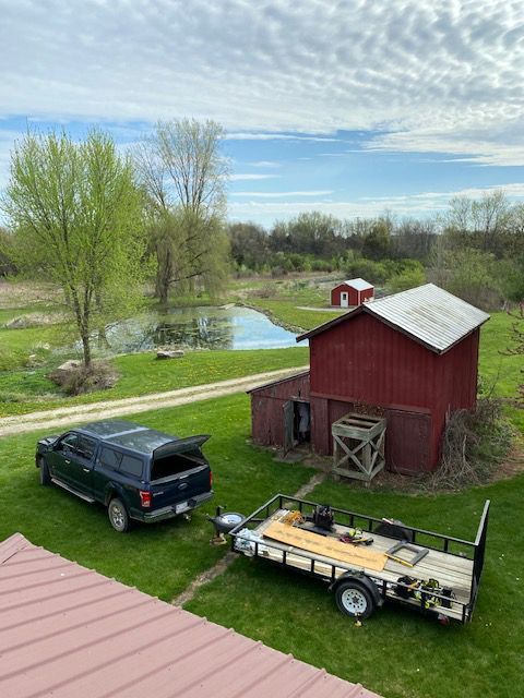 A truck is towing a trailer in front of a red barn.