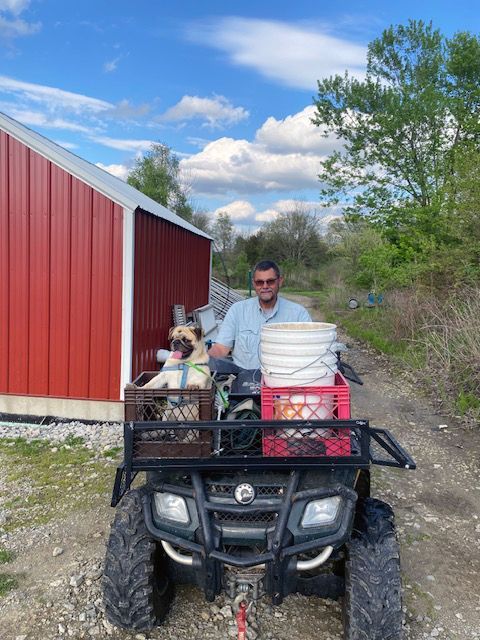 A man is sitting on a four wheeler with a dog in the back.