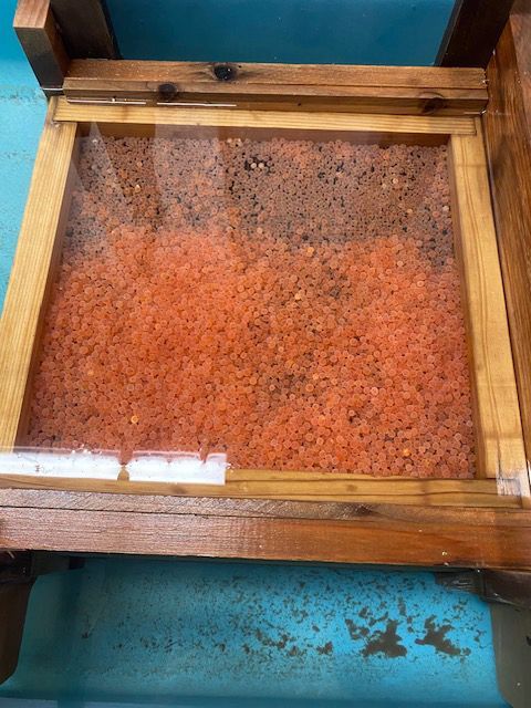 A wooden box filled with red sand is sitting on a table.