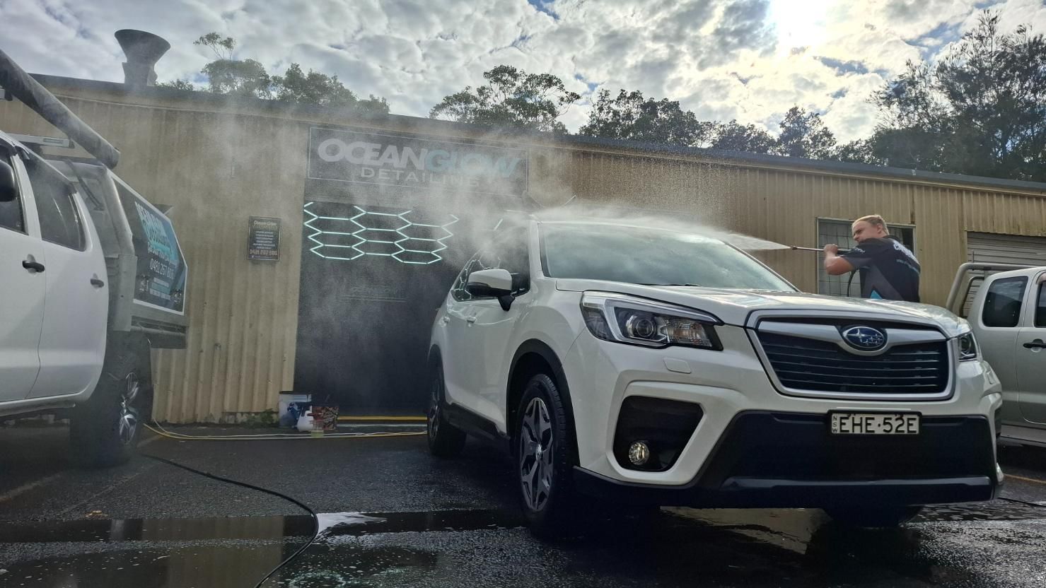 Man with pressure washer who is blasting a white four wheel drive - Ocean Glow Car Detailing in Long Jetty NSW