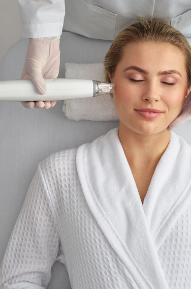 A woman in a white robe is getting a treatment on her face.