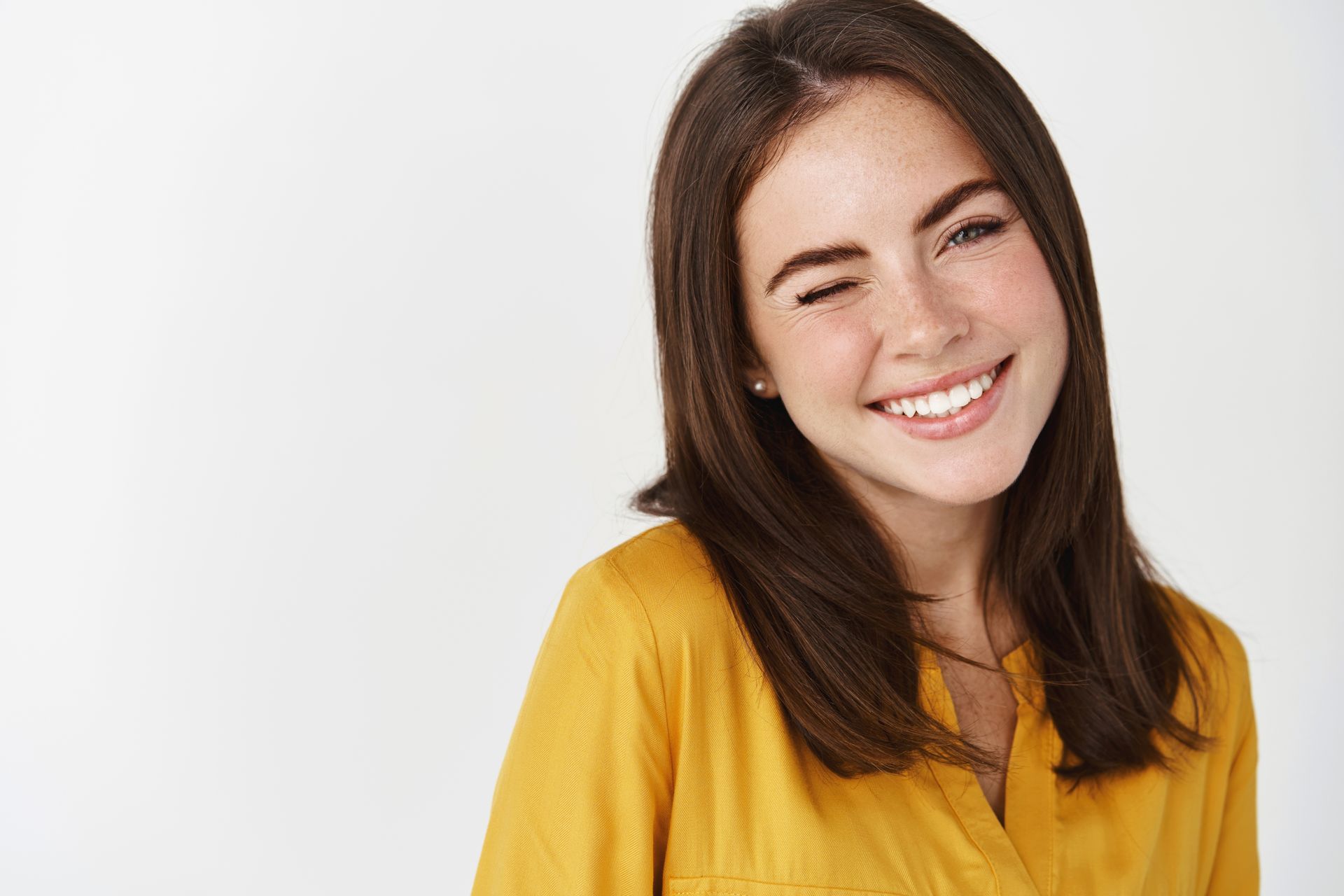 A young woman in a yellow shirt is smiling and looking to the side.