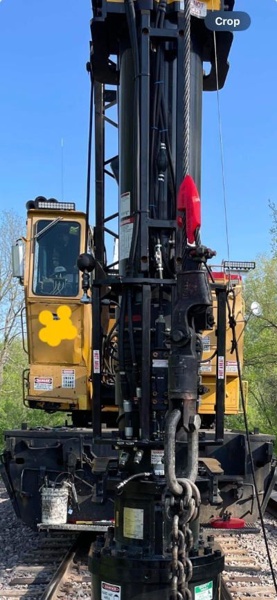 A large yellow and black machine is sitting on top of a train track has a Ropinator installed.