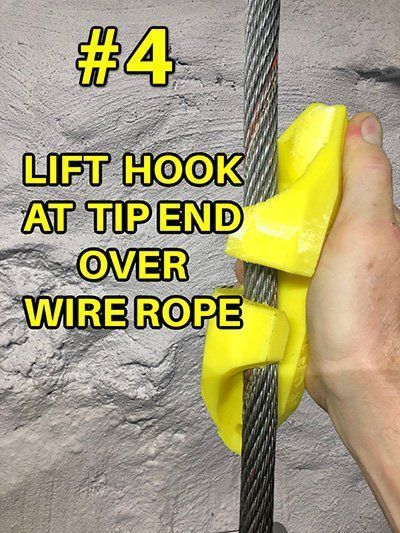 A person is holding a yellow hook over a wire rope.
