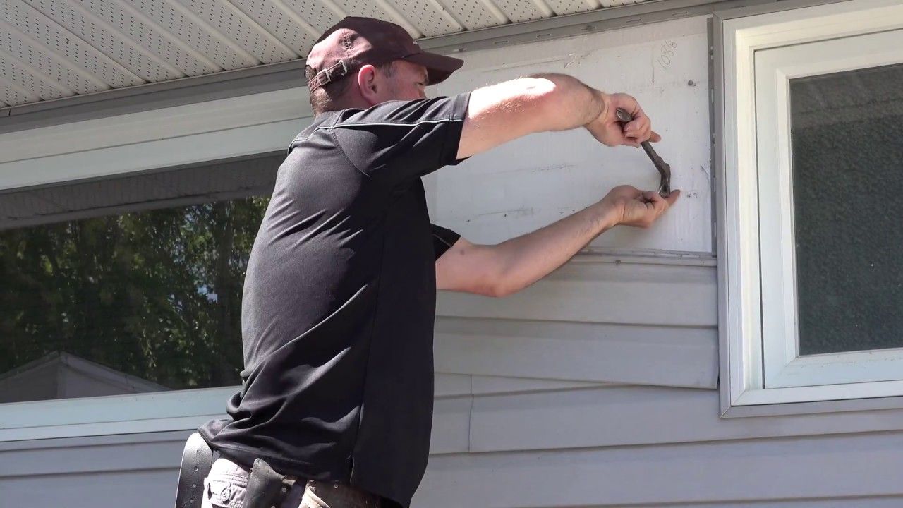 A man is working on the side of a house with a hammer.