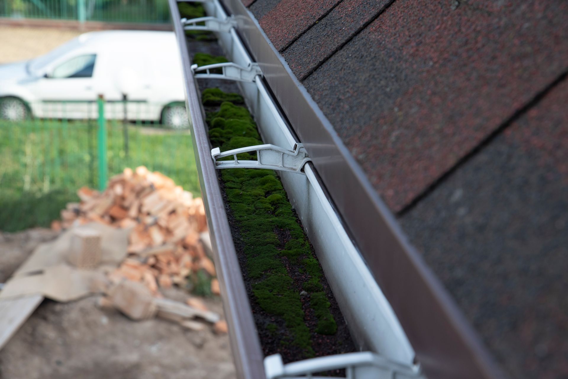 Close-up of a house gutter clogged with dirt and green moss.