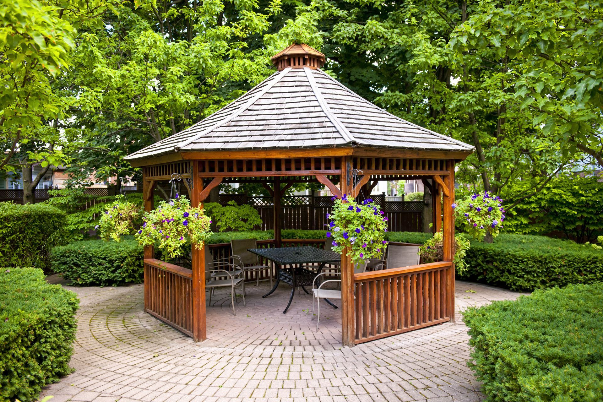 A wooden gazebo with a table and chairs in a garden.