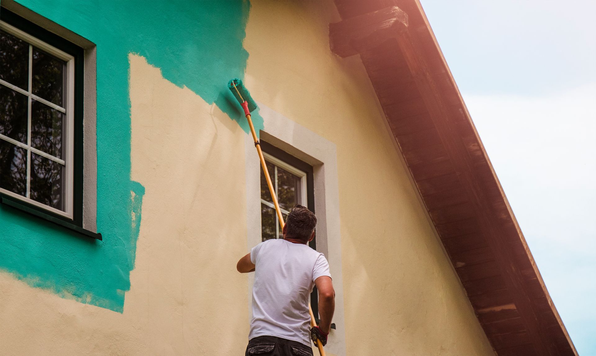 Worker painting the exterior wall of a house with a bright teal color.
