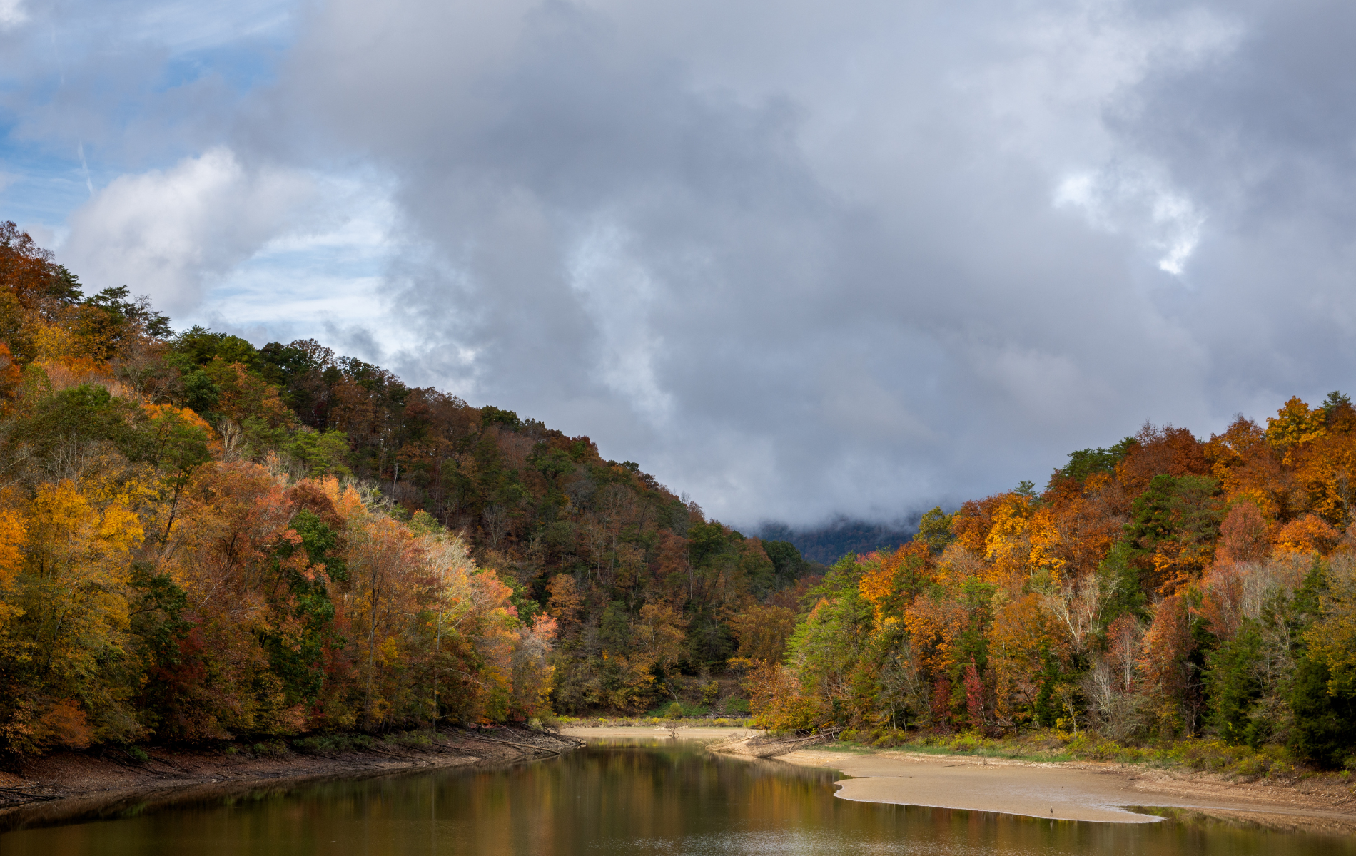 A lake surrounded by trees and mountains on a cloudy day.