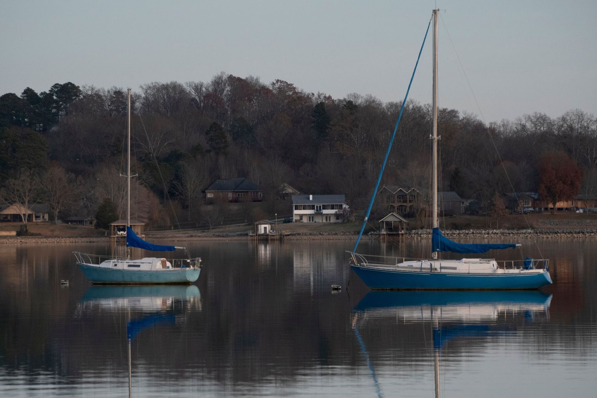 Two sailboats are floating on Fort Loudoun Lake with trees in the background