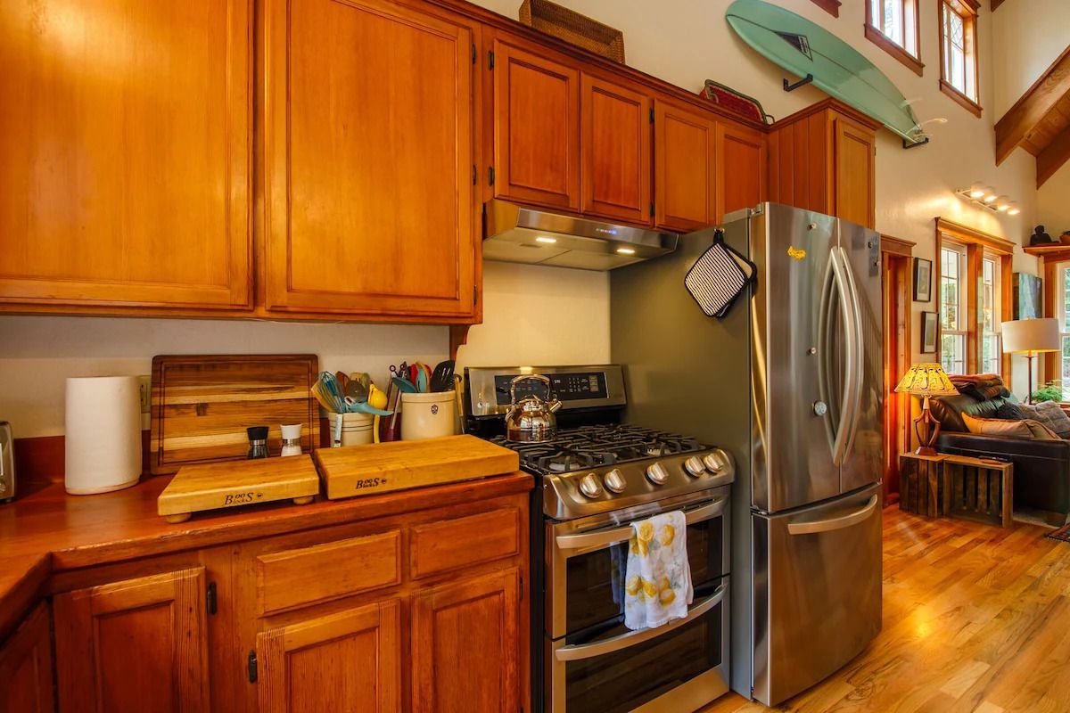 Kitchen with wooden cabinets, stainless steel appliances, and a surfboard mounted on the wall.