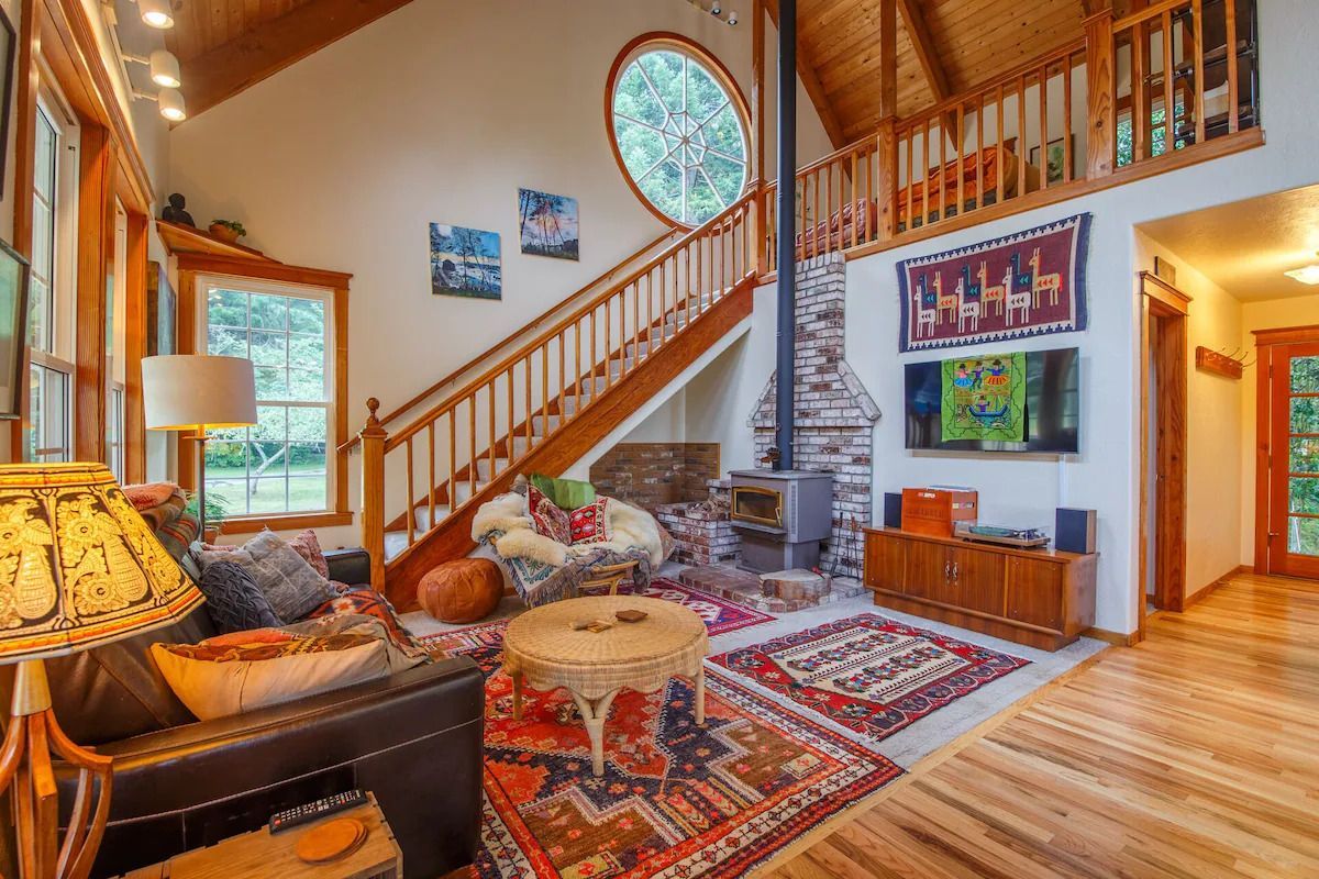 Cozy living room with wood beams, fireplace, staircase, and colorful rugs.