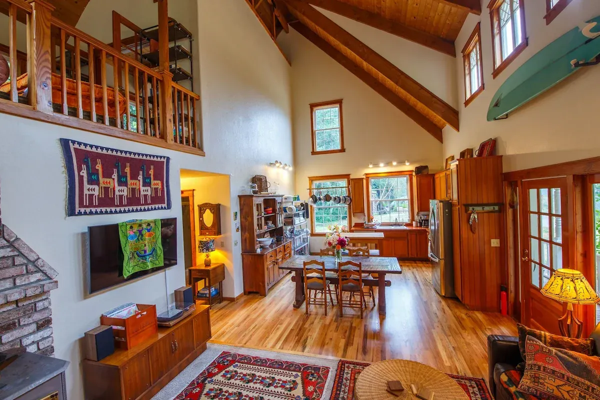 Open-concept living room with wood floors, vaulted ceiling, dining table, kitchen, and loft area.