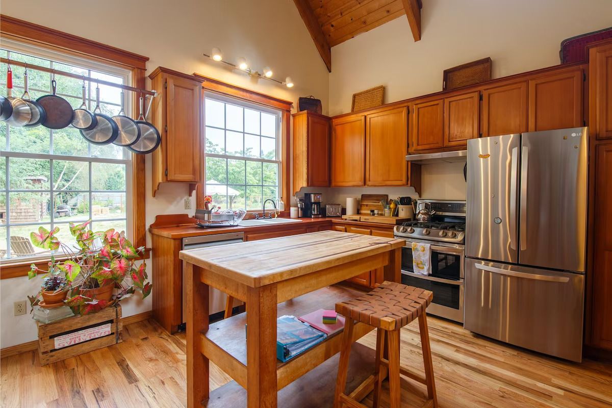 Cozy kitchen with wood cabinets, stainless steel fridge, island with butcher block top, and open windows.