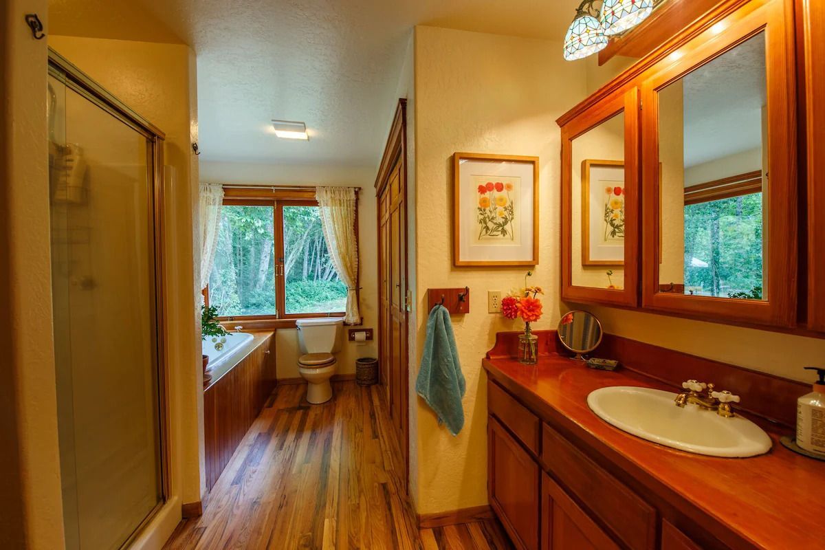 Bathroom with wooden cabinets, counter, and floor; a shower, tub, and window are visible.