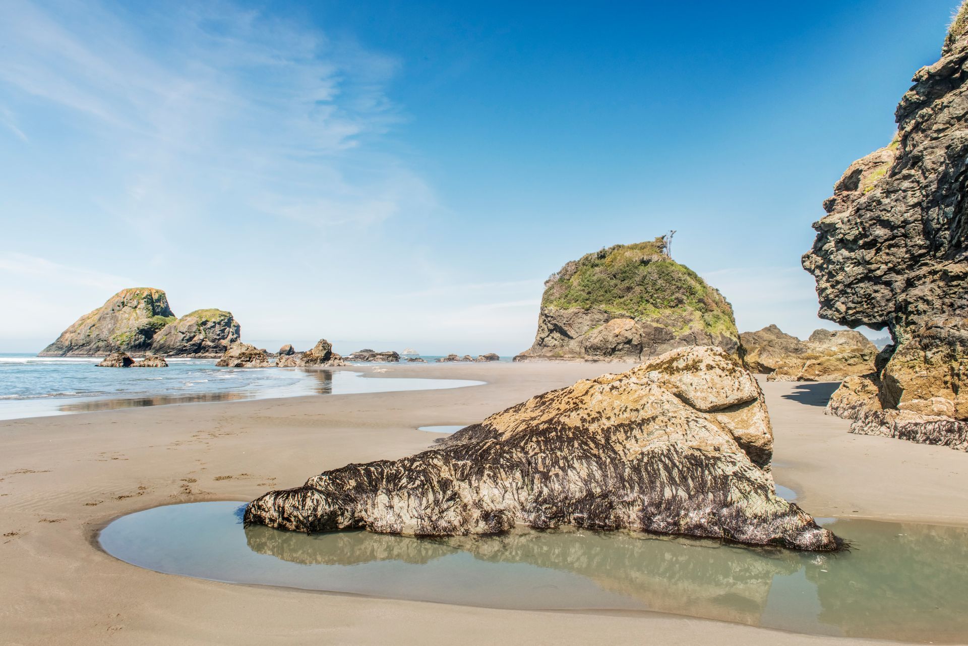 Sandy beach with large rocks, tide pools, and blue sky.