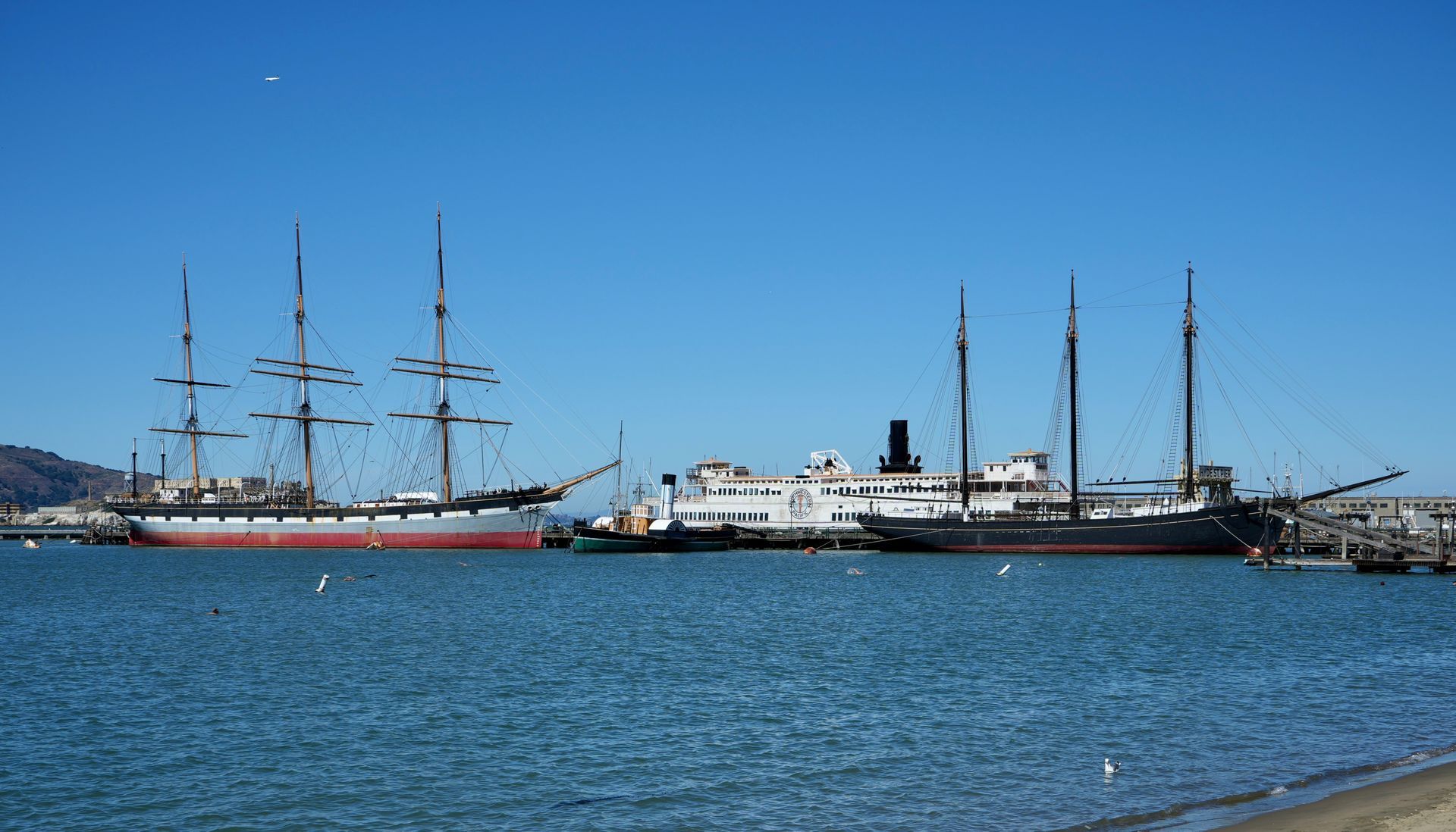 Tall ships docked in blue water under a clear sky.