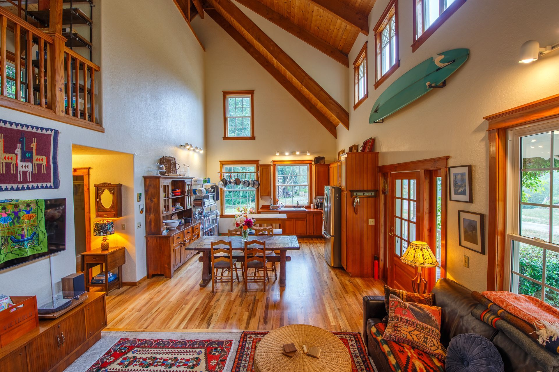Spacious living area with wooden floors, kitchen, dining table, sofa, and a surfboard on the wall.