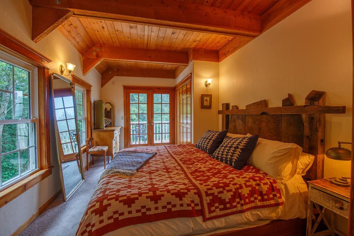 Cozy bedroom with a red quilt, wooden ceiling, and a doorway to a balcony.