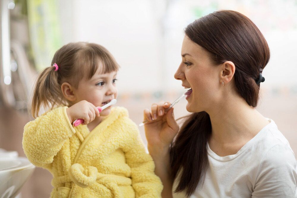 A Woman and a Little Girl Are Brushing Their Teeth Together — Dental Clinic in Buderim, QLD