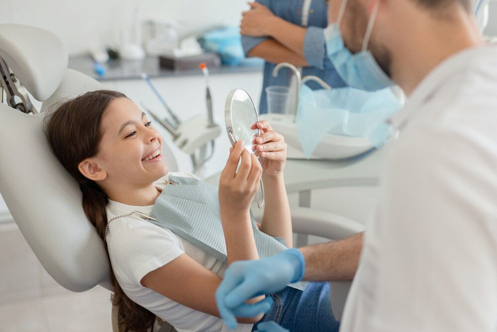 A Little Girl is Sitting in a Dental Chair Looking at Her Teeth in a Mirror  — Dental Clinic in Buderim, QLD