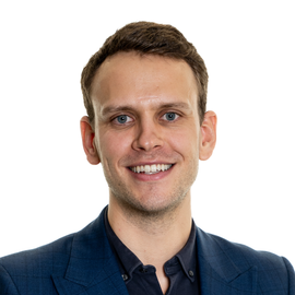 A man wearing a blue jacket and black shirt smiles for the camera