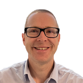 A man wearing glasses and a plaid shirt smiles for the camera