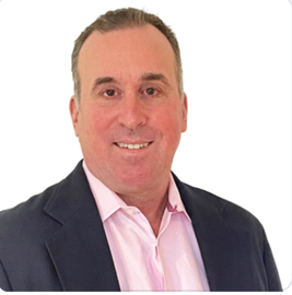 A man in a suit and pink shirt smiles for the camera