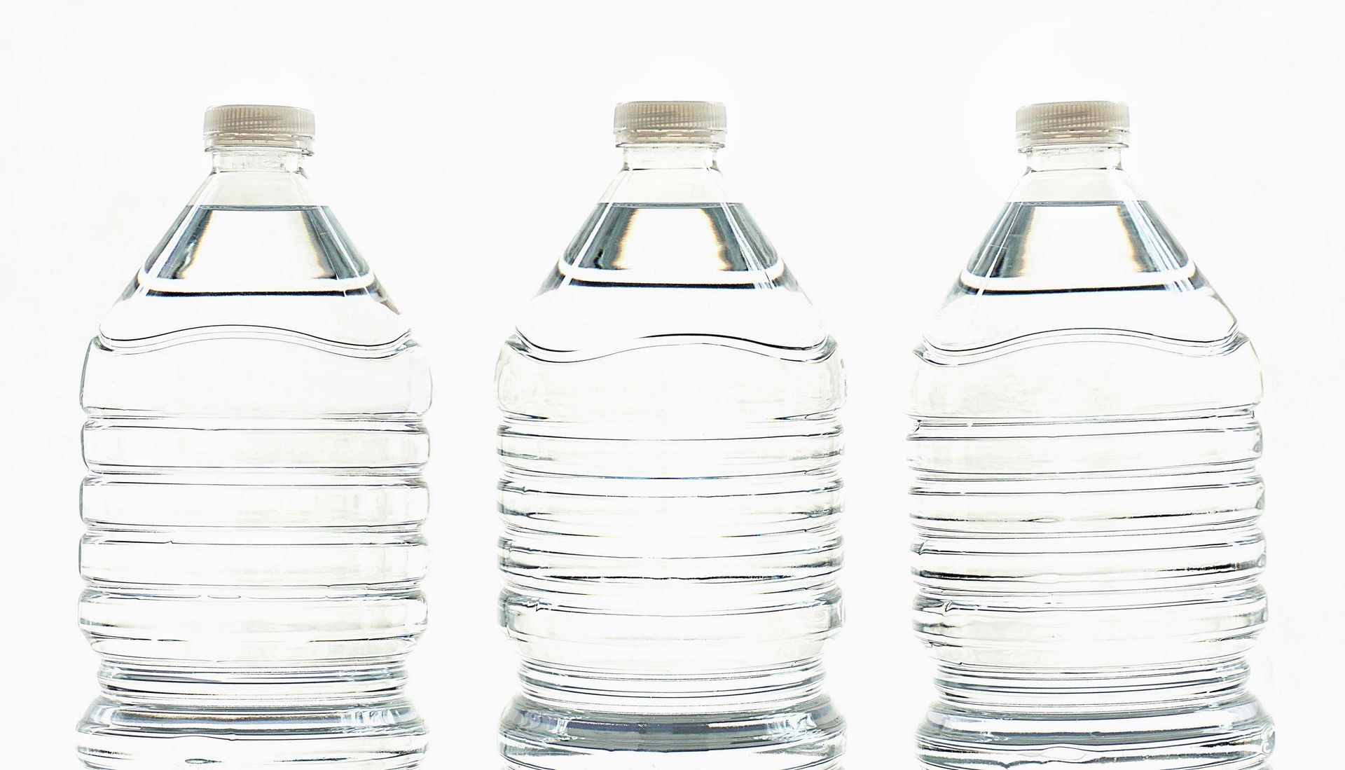 Three clear plastic water bottles, filled, against a white background.