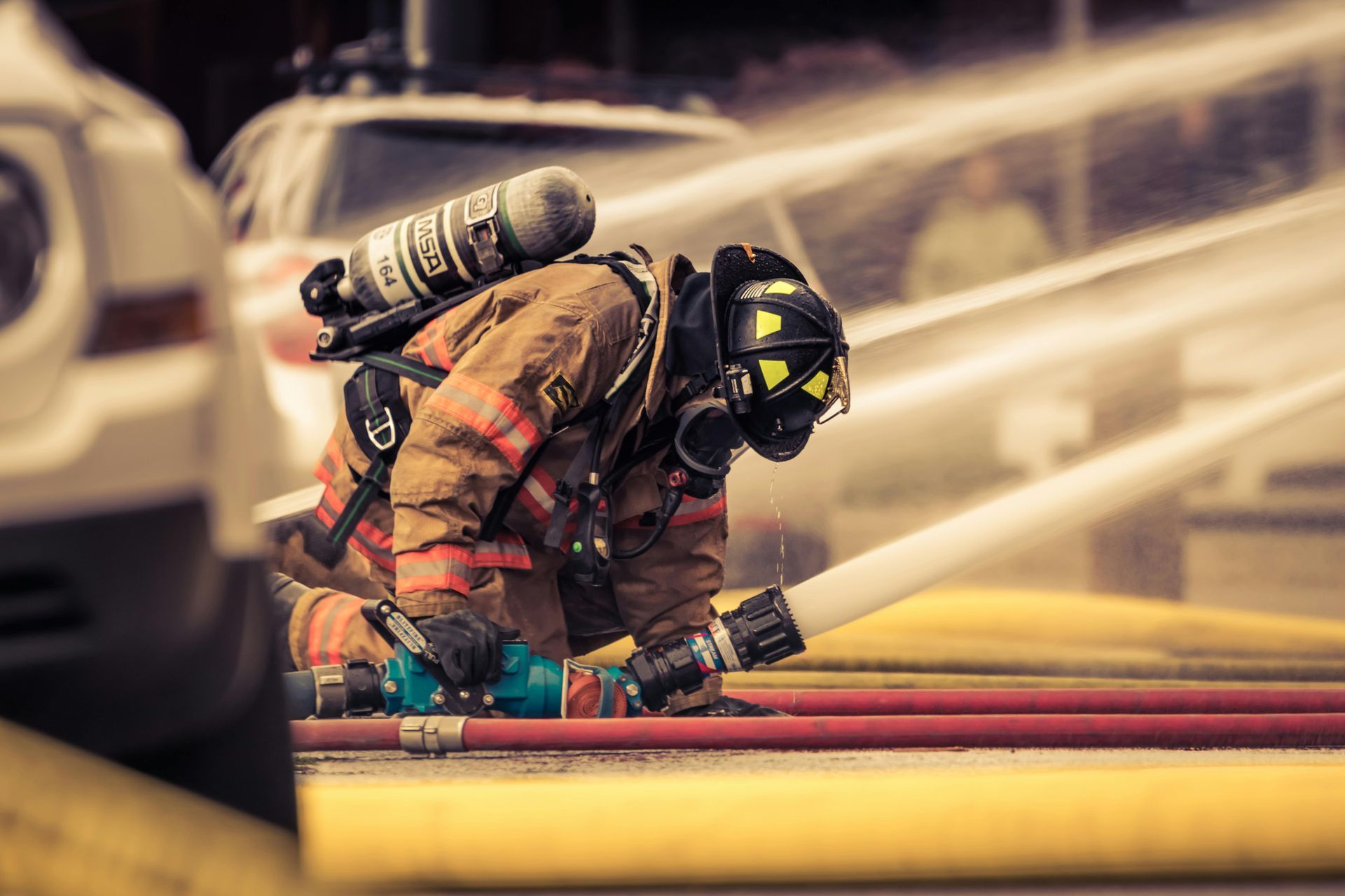 A fireman is kneeling down and spraying a fire hose.