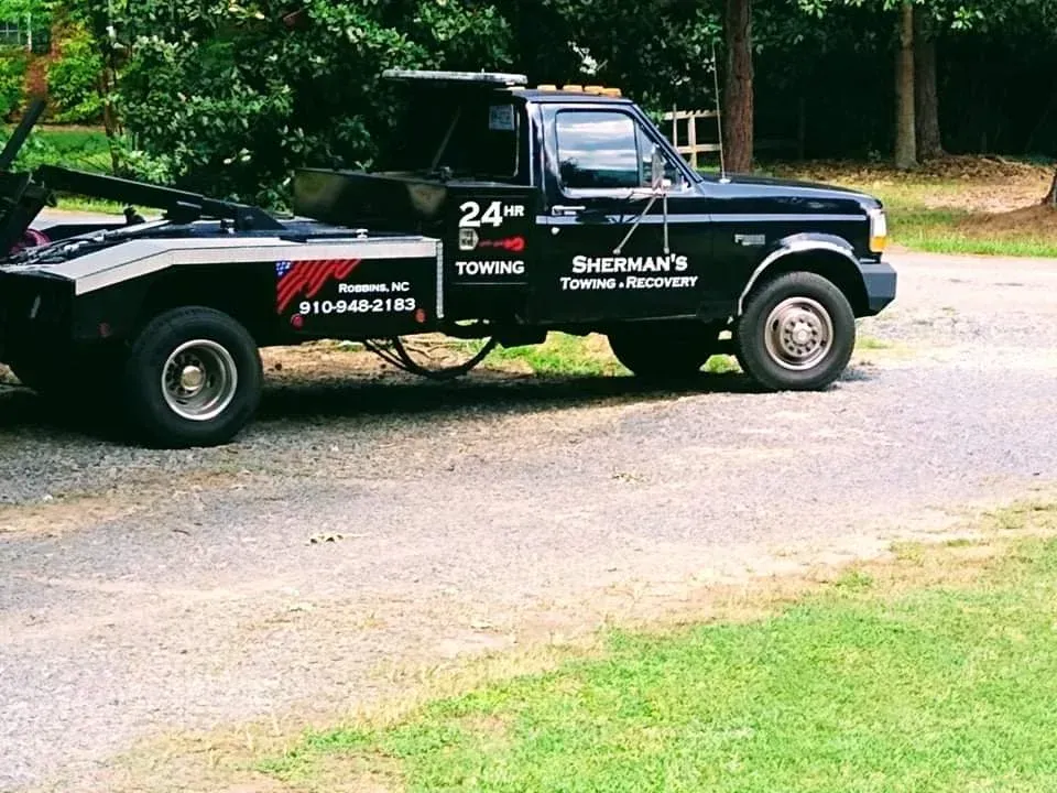 Tow truck with blue and white paint, holding a motorcycle on its flatbed, parked on a road.