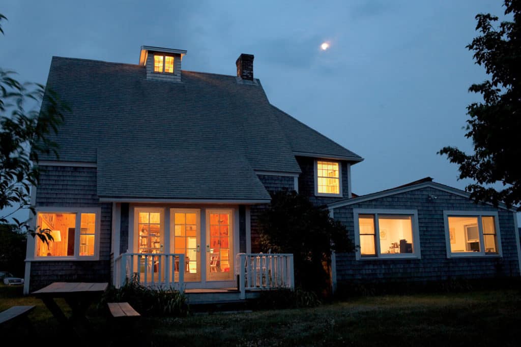 A house is lit up at night with the moon in the background