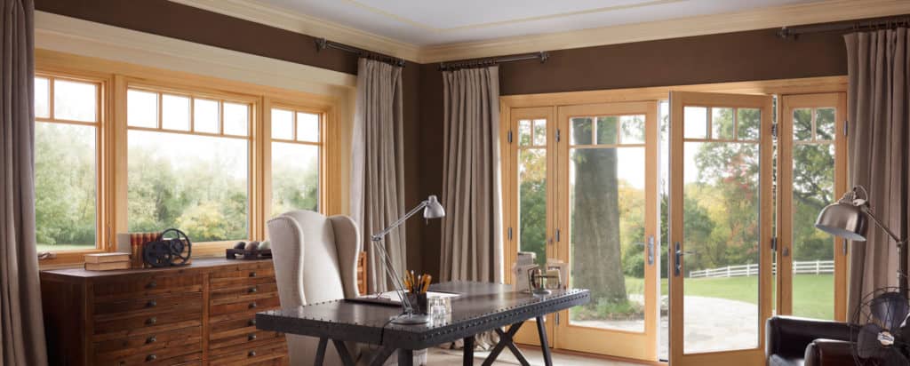 A living room with a desk , chair , lamp and sliding glass doors.
