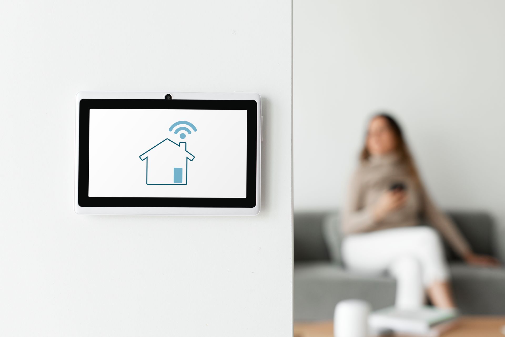 A woman is sitting on a couch in front of a smart home display.