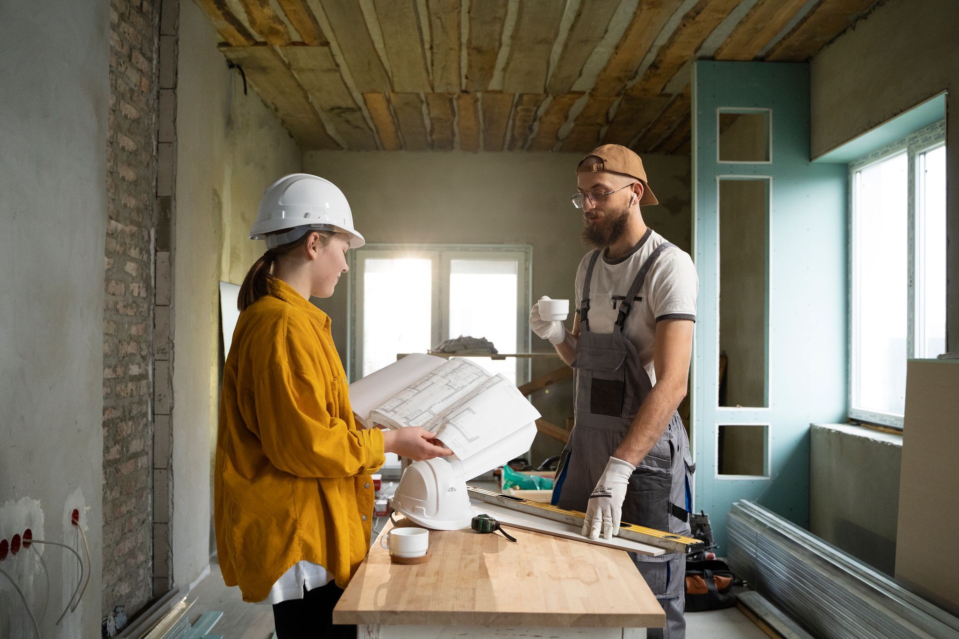 A man and a woman are looking at a blueprint in a room under construction.
