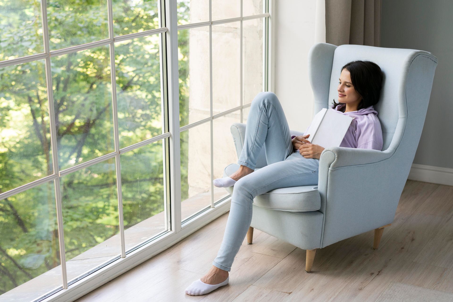 A woman is sitting in a chair looking out a window.